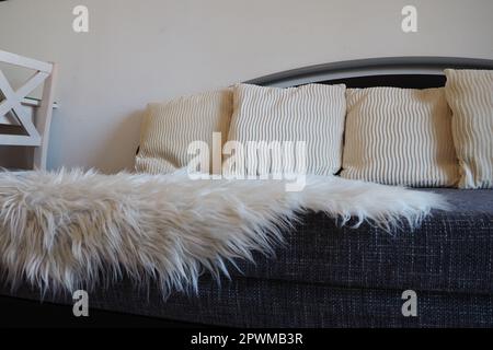 Gray sofa with boucle upholstery fabric and white decorative fluted cushions. White rug or bedspread made of faux fur with a long pile. Living room in Stock Photo