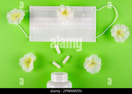 Striking juxtaposition of face mask and handful of capsule pills against  green backdrop with beautiful flowers, underscoring the need for balance in Stock Photo