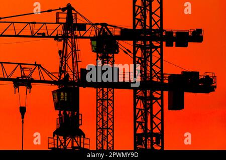 the silhouettes of construction cranes in the red-orange evening or morning sky Stock Photo