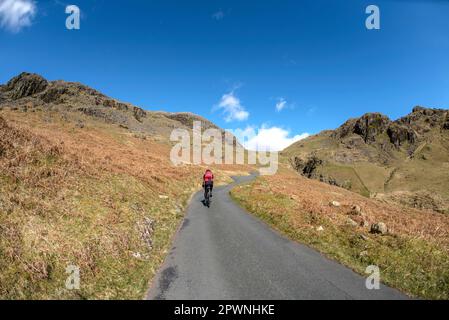 A lone road cyclist climbing the steepest road in England, Hardknott Pass, English Lake District. Stock Photo