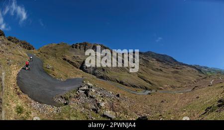 A cyclist pushes their bike up the steepest road in England, Hardknott Pass, Cumbria, UK Stock Photo