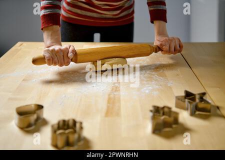Unrecognizable woman rolls out ginger dough with rolling pin on kitchen table Stock Photo