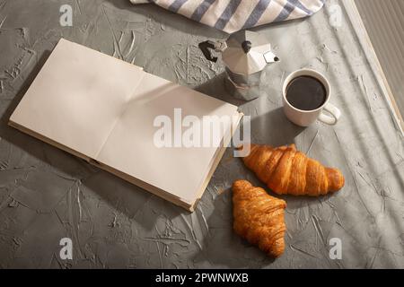 Breakfast with croissant and coffee moka pot and book with empty pages place for advertising. Morning meal and breakfast concept. Top view. Mockup. Stock Photo
