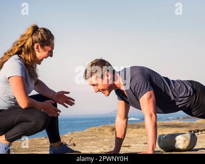 Woman with man doing push-ups on the beach of Azkorri Stock Photo