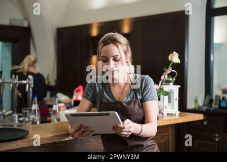 Young woman in apron using tablet at restaurant Stock Photo