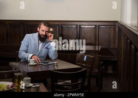Young man talking on phone while using digital tablet at restaurant Stock Photo