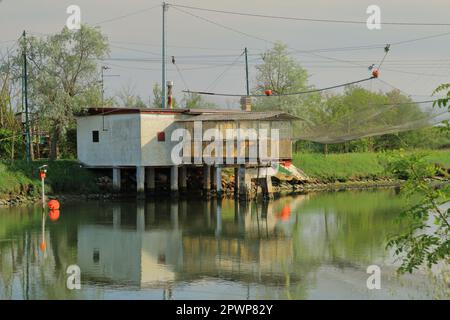 An old white fishing hut is reflected in the water of the Po Delta in Italy on a May afternoon. Stock Photo