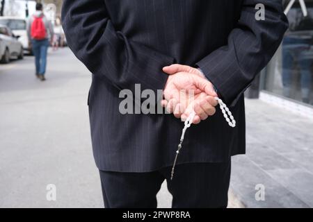 A man holding a rosary behind his back Stock Photo