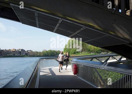 male and female joggers beside the river thames on dukes meadows footbridge, below barnes bridge on the river thames, chiswick, london, england Stock Photo