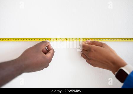 Black Man And Woman Taking Measurements With Tape Ruler On White Wall Stock Photo