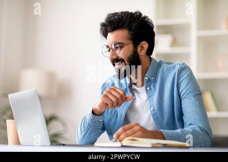 Indian man using laptop and taking notes while working at home office Stock Photo
