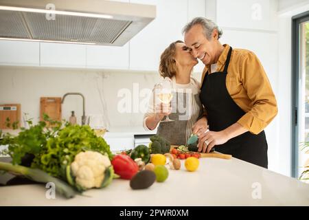 Loving senior spouses cooking together, woman kissing her husband, preparing dinner at cozy kitchen, free space Stock Photo