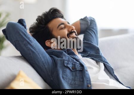 Home Comfort. Portrait Of Relaxed Young Indian Man Leaning Back On Couch Stock Photo