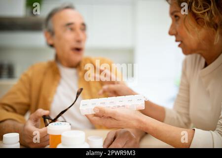 Senior man and woman taking medicine in morning, wife giving daily pills to her husband, kitchen interior Stock Photo