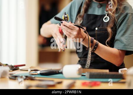 Woman using rotary punch tool for making holes in leather belt Stock Photo