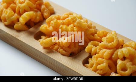 Cheetos is a crunchy corn puff snack. Bright orange cheese puffs in a wooden board. Stock Photo