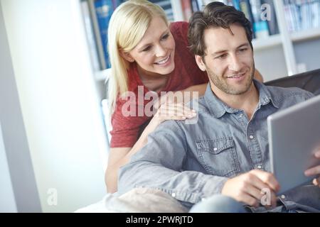 Saying hello to the in-laws. a young man using a digital tablet while his girlfriend watches from behind. Stock Photo