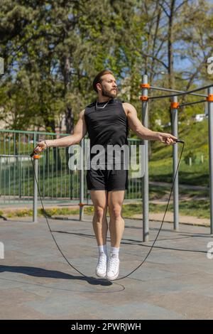 Athletic lebanese man in sportswear skipping rope. Young middle eastern arabian guy doing jumping exercises on playground. Sports crossfit, fitness routine, workout. Strength motivation. Outdoors Stock Photo