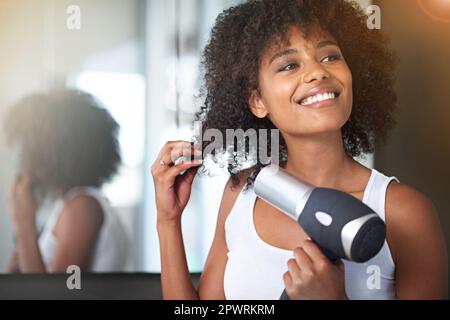 Making sure she has a great hair day. a young woman blow drying her hair in the bathroom. Stock Photo