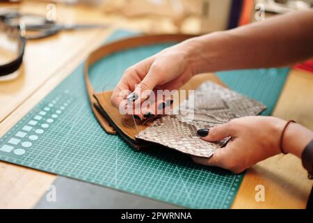 Hands of leather worker sewing parts of leather bag together Stock Photo