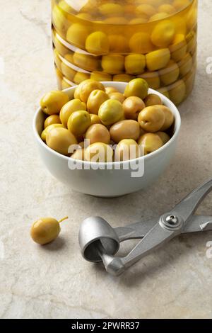 Bowl with green Turkish olives close up  and a metal olive pitter and an olive in front Stock Photo