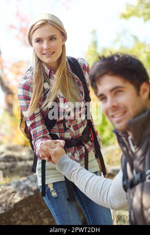 Letting him lead her down. A handsome young hiker helping his girlfriend as they hike down a mountainside. Stock Photo