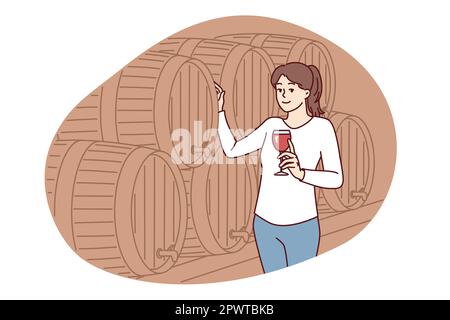 Woman with glass of wine stands near wooden barrel for tincture of alcoholic drink and looks at screen. Positive lady in casual clothes walking alone Stock Photo