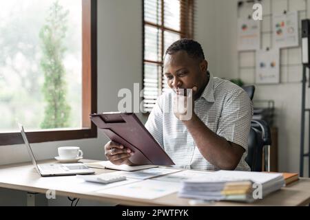 Black business man doing paperwork at home workplace. Entrepreneur reading financial reports, reading documents. Tenant making payment for rent Stock Photo