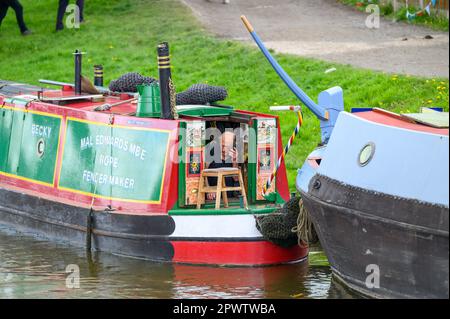 Man making a phone call on a mobile phone while sitting in the aft cabin door of a traditional narrowboat moored on the canal at Norbury. Stock Photo