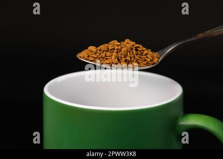 Close-up of a teaspoon with granulated instant coffee over a mug, macro. Stock Photo