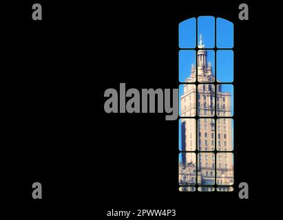 View from inside big window grid looking out at a traditional skyscraper building on blue sky copy space. Dark room with light part of a gothic vintag Stock Photo