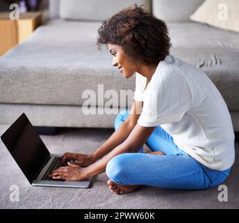 Checking out the latest celeb news. a young woman sitting on the floor with her laptop at home. Stock Photo
