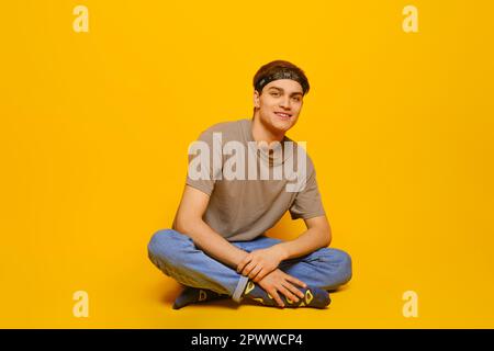 Happy young man in everyday clothes sitting on the floor in bright yellow studio Stock Photo