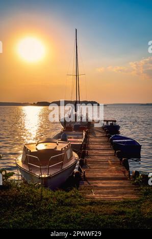 Sailing yacht and jetty in the beautiful lake. Empty wooden jetty with moored boats on the lake shore at the sunrise in Mazury region, Poland. Stock Photo