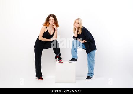 Two teen girls lean on square box over white studio background Stock Photo