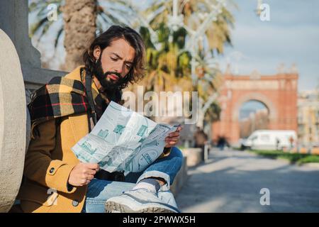 One bearded tourist male reading a map to found some monument location visiting Barcelona. An adult traveler man looking for directions on a guide , sightseeing on a Europe journey trip. High quality photo Stock Photo