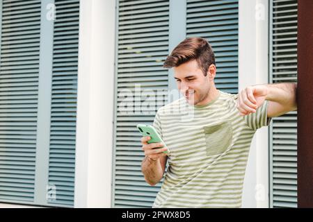 Young happy male browsing on internet using a cellphone device standing outdoors. One teenager smiling and typing on a social media with a smart phone app. Guy chatting and sending messages by phone. High quality photo Stock Photo