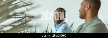 Smiling african businessman working on computer sitting in coworking on colleagues background Stock Photo