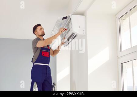 Young man repairing air conditioner standing on stepladder Stock Photo