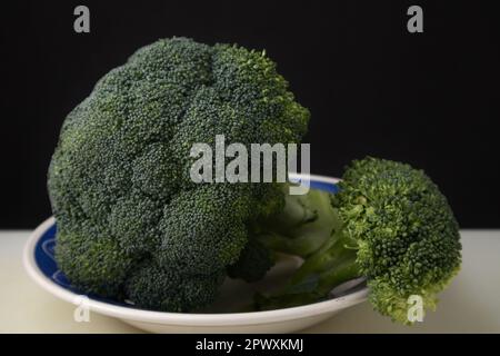 Close-up of a fresh broccoli cabbage in a plate on a light table against a dark background with copy space Stock Photo