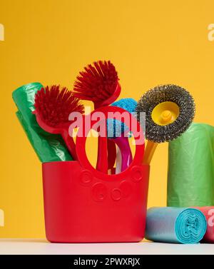 Plastic basket with brushes, disinfectant in a bottle on a yellow background. House cleaning items set Stock Photo