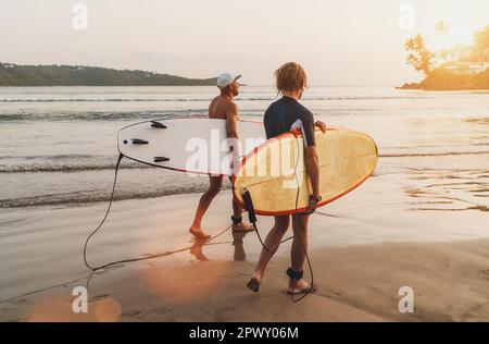 Father with teenager son with surfboards walking by sandy ocean beach on Sri Lanka island. They have a winter vacation and enjoying a beautiful sunset Stock Photo