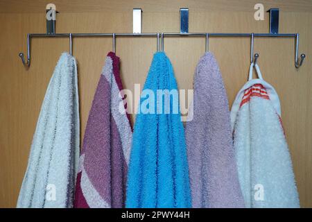 White, blue, pink towels hanging from metal hooks attached to the bathroom door. The situation in the bathroom or toilet, kitchen. Housekeeping. Hygie Stock Photo