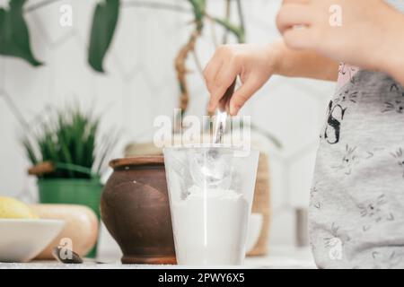 Hands of little girl bake apple pie in kitchen. Child puts flour in measuring cup. Children help on household chores. Kid cooking food. Top view Stock Photo