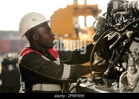 Side view of young male engineer in workwear checking hydraulic hoses and other details of indistrial machine while working in factory Stock Photo