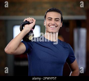 Fitness, portrait or man at gym with a kettlebell for strong arms or training biceps in workout or weightlifting exercise. Smile, face or happy person Stock Photo