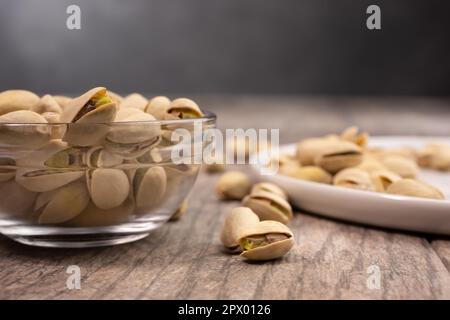 A view of pistachio nuts in a clear glass bowl and on a white plate. Stock Photo