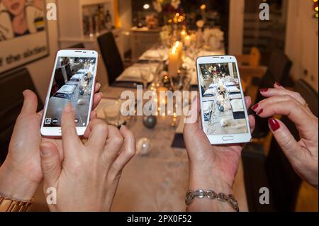 Two women hands with smartphones photographing a festively set and decorated Christmas table Stock Photo