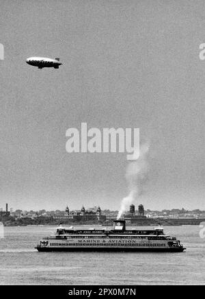 AJAXNETPHOTO. JULY, 1975. NEW YORK HARBOUR, USA. - GOODYEAR BLIMP - AIRSHIP SAILS OVER STATEN ISLAND FERRY WHICH IS EN-ROUTE TO BATTERY, MANHATTAN, WHILE PASSING OLD ELLIS ISLAND IMMIGRATION CENTRE (BACKGROUND).PHOTO:JONATHAN EASTLAND/AJAX REF:232404 113 Stock Photo