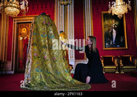 Caroline de Guitaut, deputy surveyor of the King's Works of Art for the Royal Collection Trust, adjusts the Imperial Mantle, which forms part of the Coronation Vestments, displayed in the Throne Room at Buckingham Palace, London. The vestments will be worn by King Charles III during his coronation at Westminster Abbey on May 6. Picture date: Wednesday April 26, 2023. Stock Photo